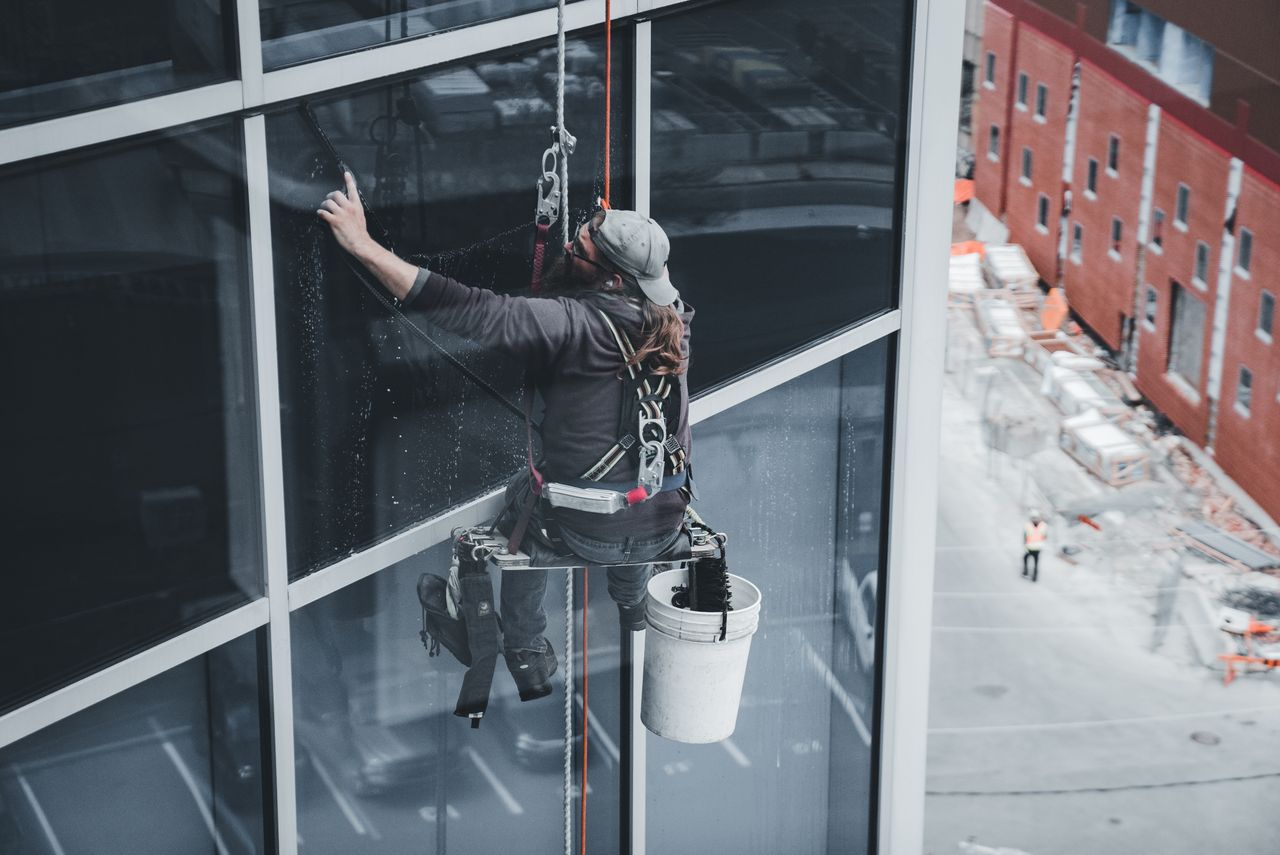 Un agent nettoie les vitres d’un gratte-ciel, harnaché, dans un environnement urbain.