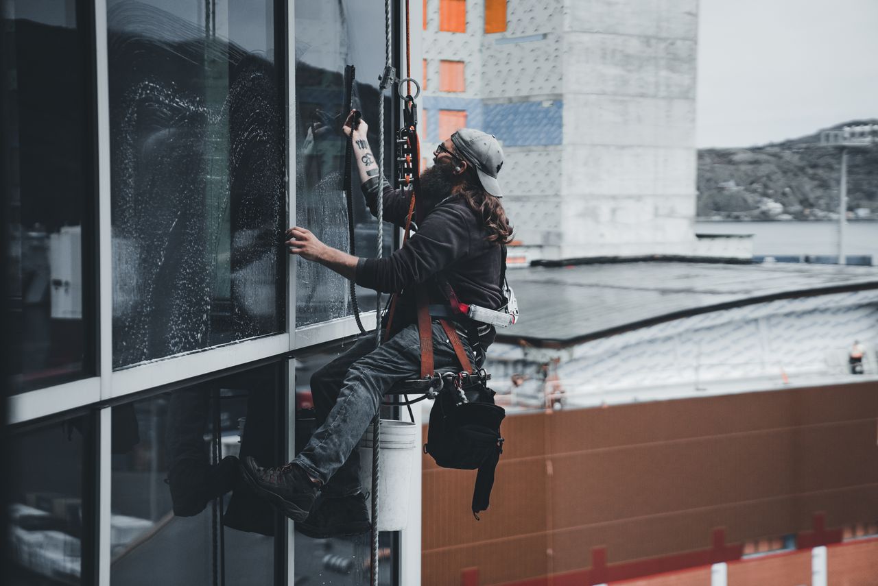 Un homme nettoie les vitres d'un gratte-ciel avec un harnais, illustrant un travail en hauteur en milieu urbain.